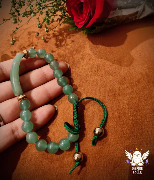 green aventurine bracelet with gold accents held by a hand on a brown surface, with flowers in the background.