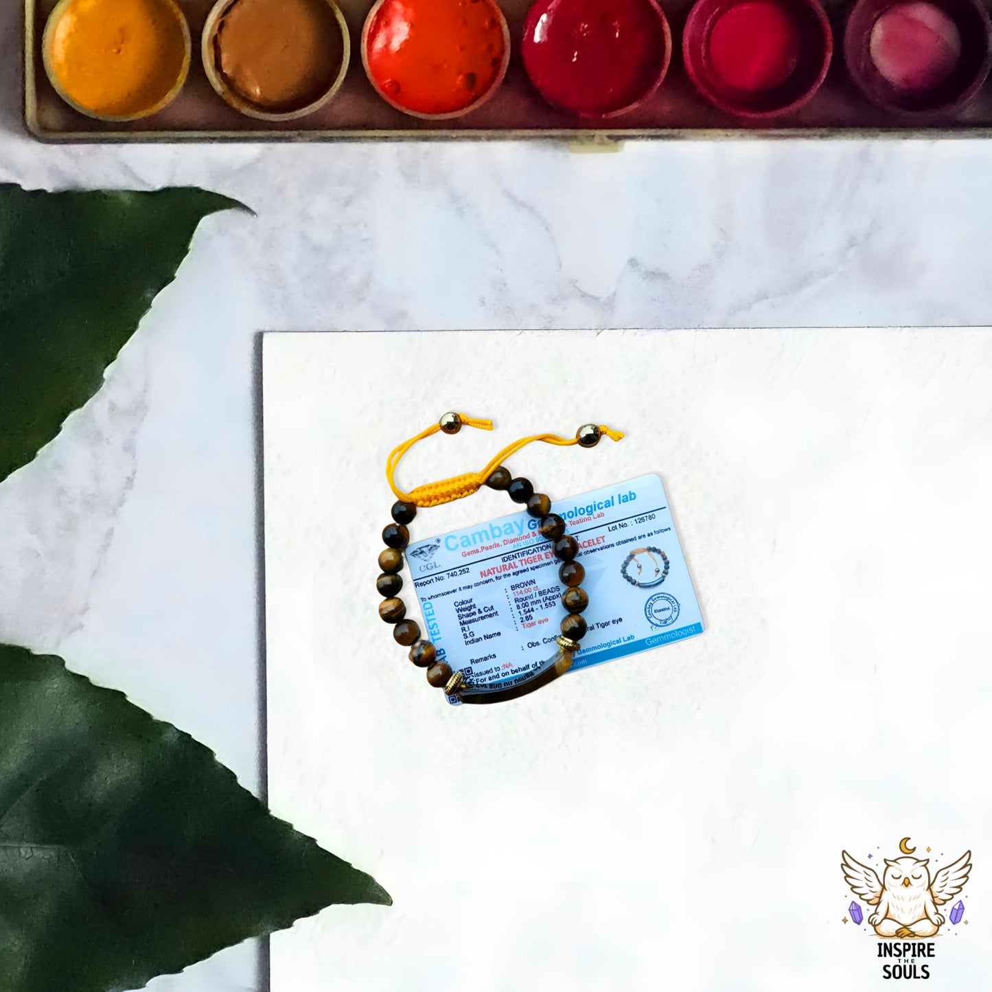 tiger eye Bracelet with certification card on a white surface, surrounded by watercolor paints.