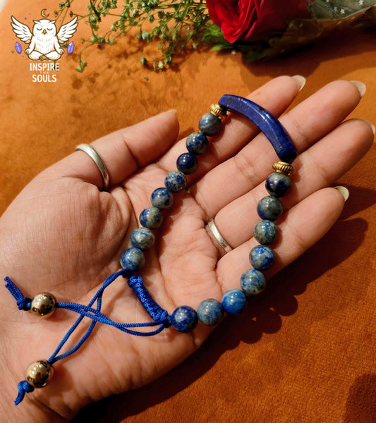 Hand holding a lapis lazuli blue beaded bracelet with gold accents on a wooden surface.