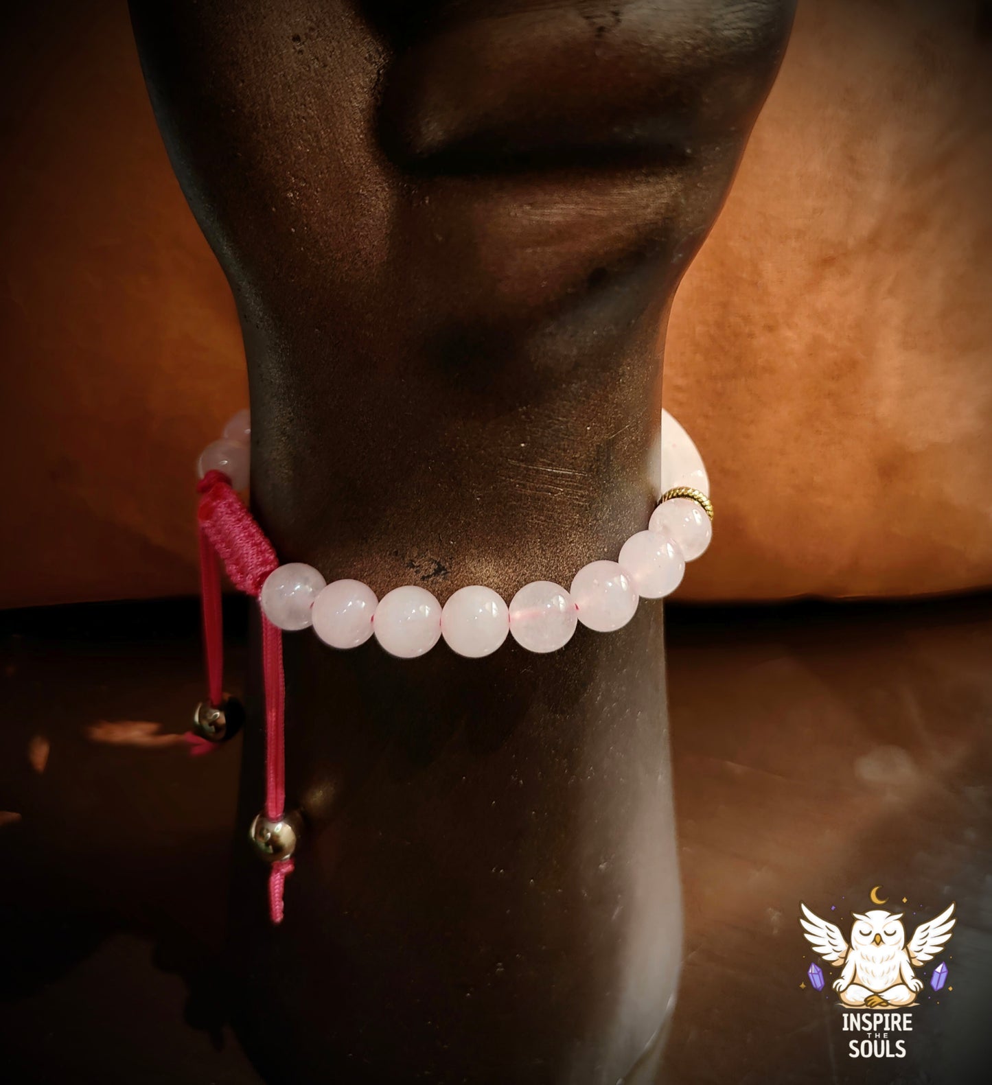 Close-up of a horse's leg wearing a rose quartz pink beaded bracelet with gold accents on a brown background.