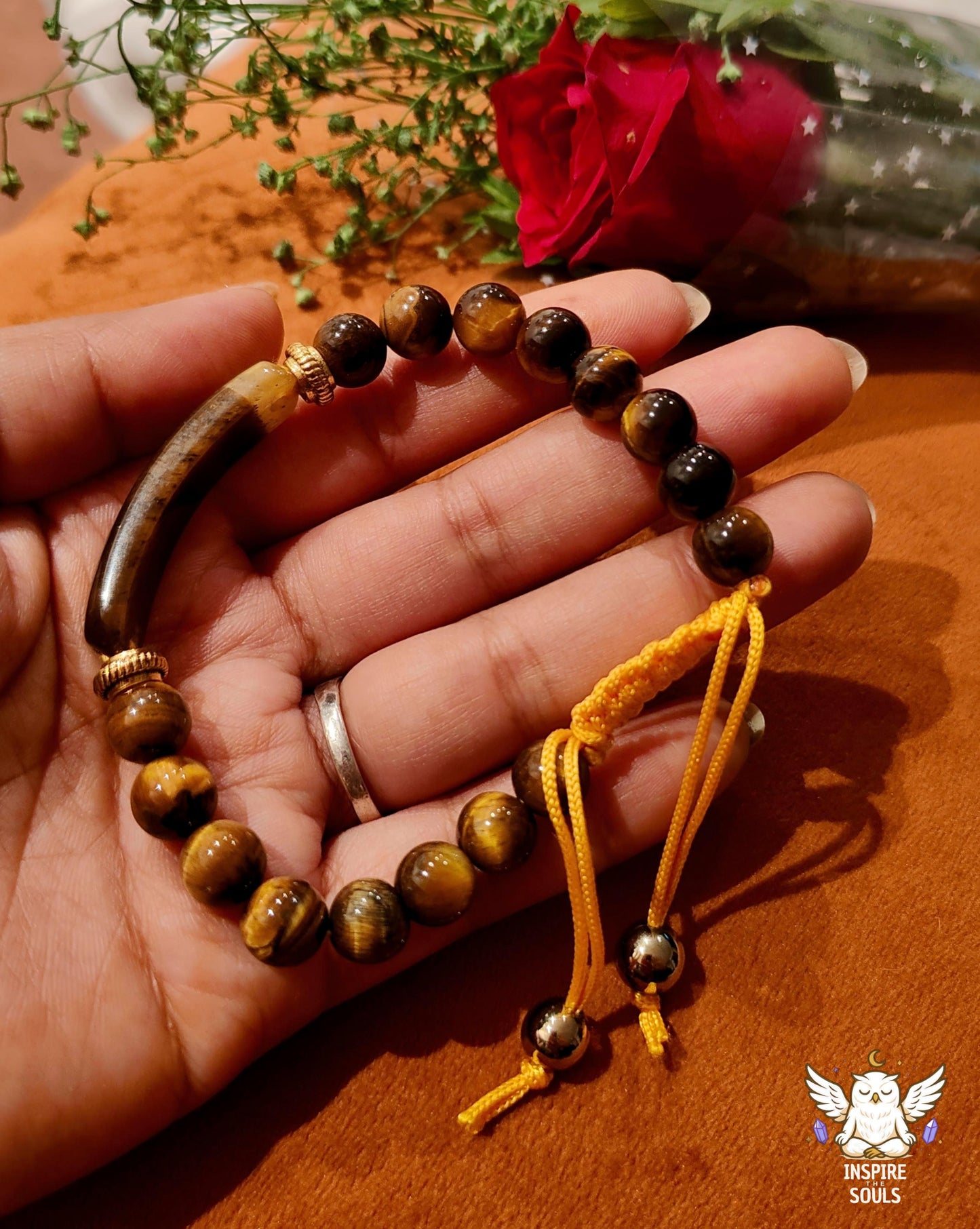 Hand holding a tiger eye soulstone series by Inspirethesouls bracelet with a yellow cord on a wooden surface and rose
