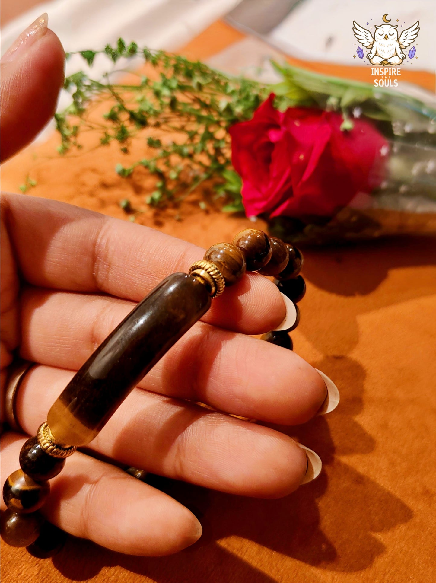 Hand holding a tiger eye soulstone series by Inspirethesouls bracelet with a red flower in the background